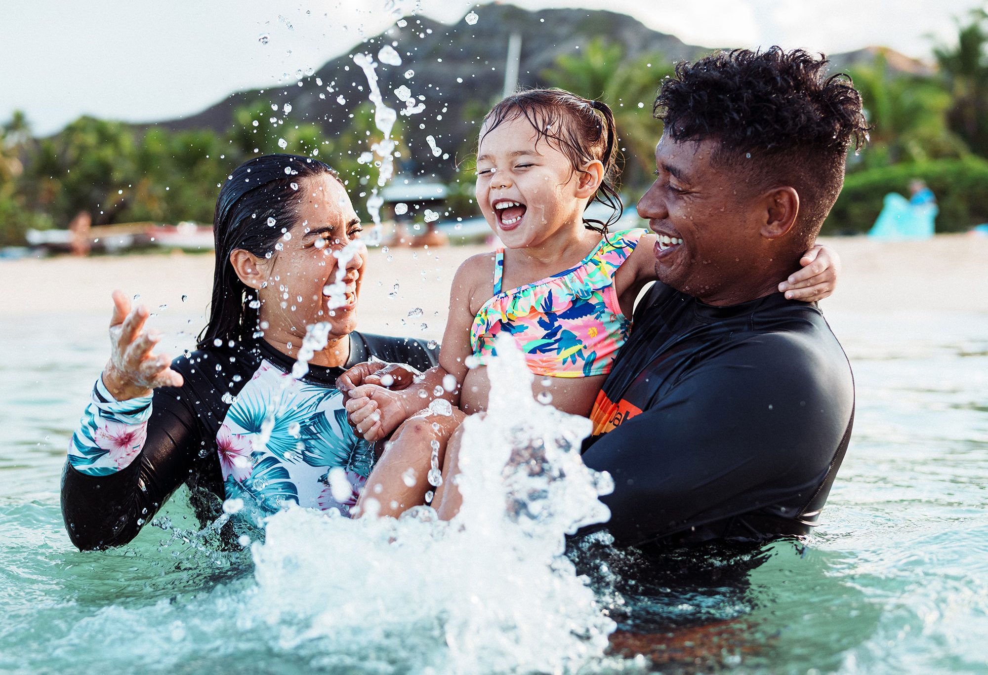 happy young family splashing around in the ocean, happy family in water, FHA refinance, Happy couple and child on vacation using savings from FHA refinance
